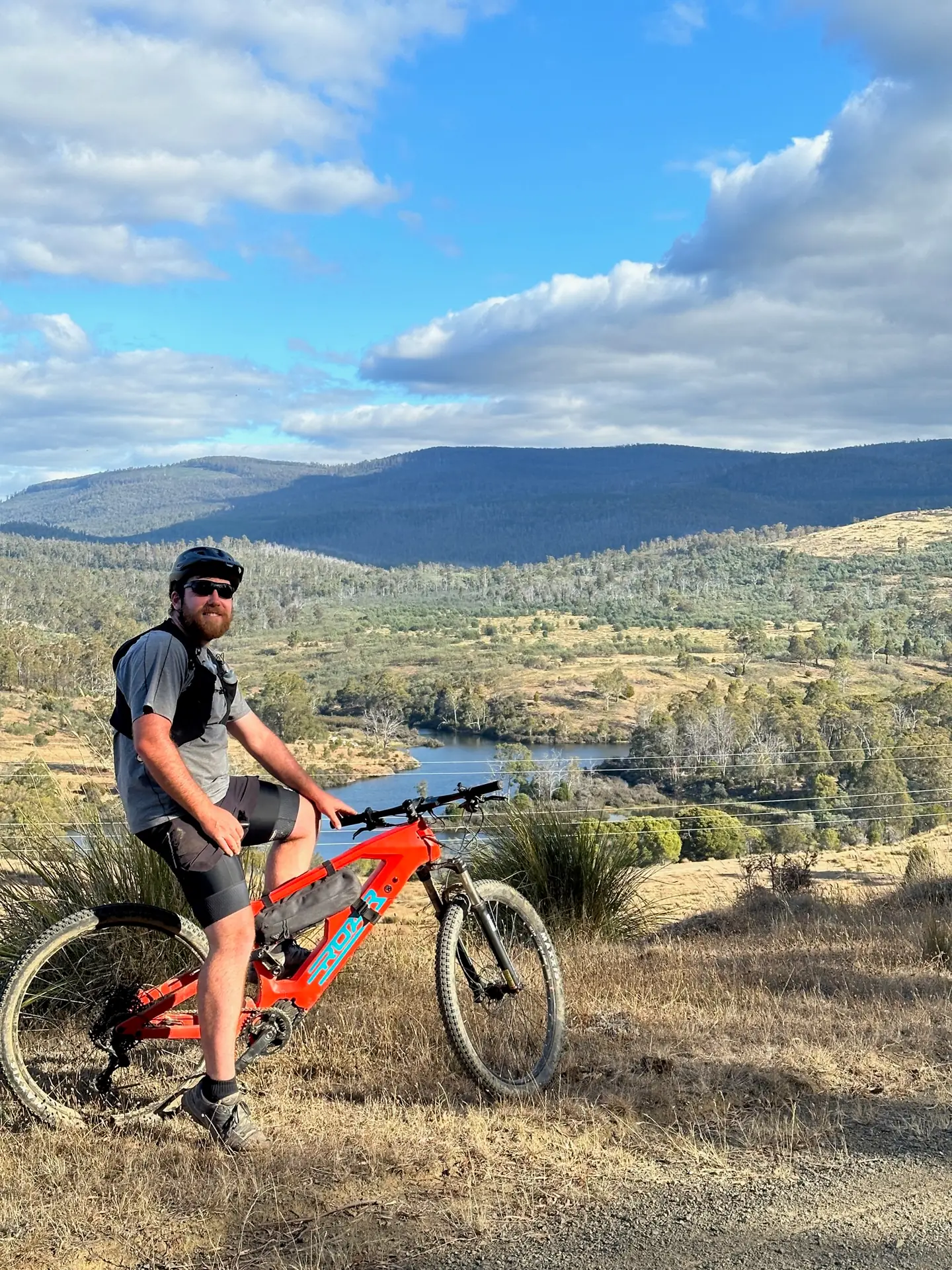 A rider with a red Roar development bike overlooking open country and a small lake.